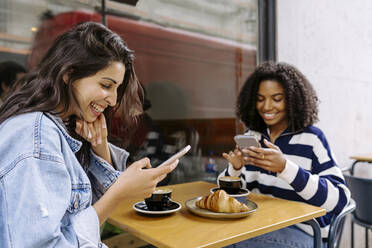 Happy young friends using smart phone sitting at table of sidewalk cafe - JJF00518