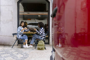 Frauen, die ein Smartphone benutzen, sitzen am Tisch eines Straßencafés - JJF00519