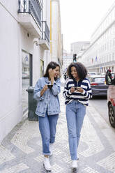 Glückliche junge Freunde mit Kaffeetassen auf dem Fußweg - JJF00521