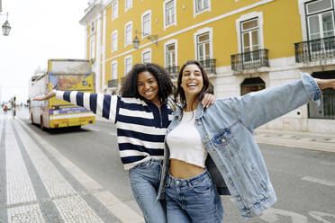Cheerful young friends enjoying on road in front of yellow building - JJF00528