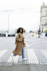 Lächelnde junge Frau beim Überqueren der Straße in der Stadt - JJF00532