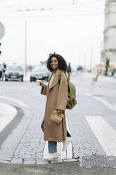 Lächelnde junge Frau mit Kaffeetasse beim Überqueren der Straße - JJF00533