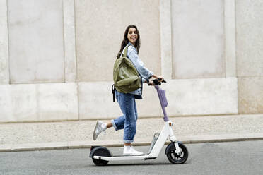 Happy young woman riding electric push scooter - JJF00544