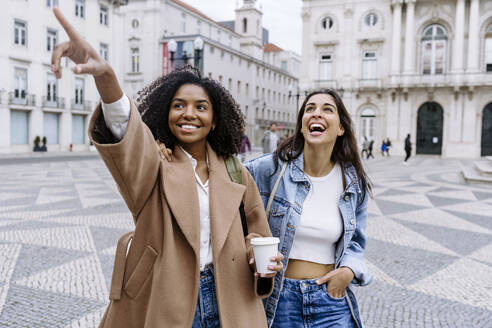 Smiling young woman gesturing and standing with friend in town square - JJF00563