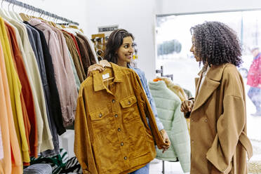 Happy young woman with friend shopping at clothing store - JJF00564