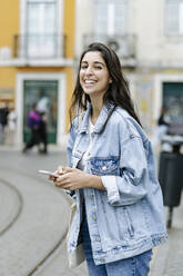 Happy young woman with smart phone standing in city - JJF00575