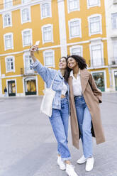 Glückliche junge multiethnische Freunde, die ein Selfie vor einem gelben Gebäude machen - JJF00584