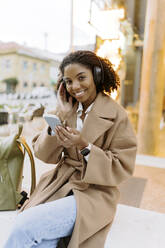 Happy young woman listening to music through wireless headphones - JJF00611