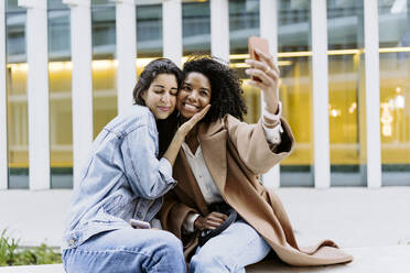 Happy young friends taking selfie through smart phone in front of building - JJF00630