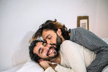 Gay man kissing boyfriend lying on bed at home - GDBF00043