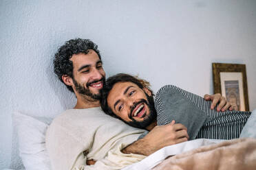 Happy gay couple relaxing together on bed at home - GDBF00044