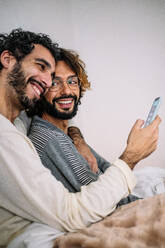 Happy gay couple with mobile phone at home - GDBF00050