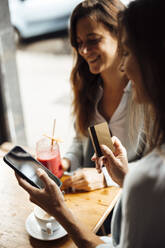 Frau mit Kreditkarte, die ein Smartphone von einem Freund in einem Café benutzt - JOSEF17559