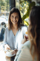 Happy woman having coffee with friend in cafe - JOSEF17563