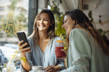 Glückliche Frau teilt ihr Smartphone mit einem Freund in einem Café - JOSEF17568