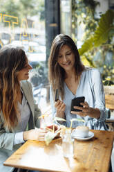 Woman with friend holding credit card using smart phone in cafe - JOSEF17573