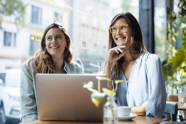 Lächelnde Geschäftsfrauen sitzen mit Laptop am Tisch in einem Café - JOSEF17576