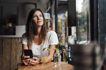 Nachdenkliche Frau sitzt mit Smartphone in einem Cafe - JOSEF17597