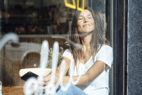 Lächelnde Frau genießt das Sonnenlicht durch Glas gesehen - JOSEF17601