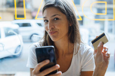 Frau mit Kreditkarte und Smartphone in der Hand, die sich in einem Café verzieht - JOSEF17612