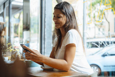 Lächelnde Frau, die in einem Café eine Textnachricht über ihr Smartphone verschickt - JOSEF17614