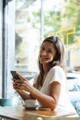 Glückliche Frau mit Mobiltelefon im Café sitzend - JOSEF17615