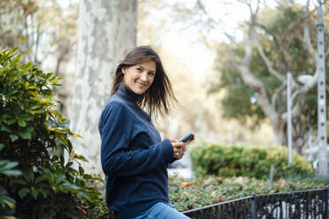 Smiling woman using smart phone by plants - JOSEF17646