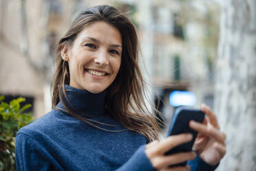 Glückliche Frau mit Rollkragenpullover und Smartphone - JOSEF17648