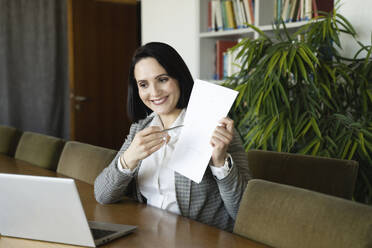 Businesswoman showing document on video call through laptop at office - NJAF00286