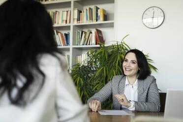 Lächelnde Geschäftsfrau im Gespräch mit einem Kollegen am Schreibtisch im Büro - NJAF00289