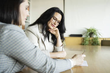 Businesswoman discussing with colleague over document in meeting at office - NJAF00294