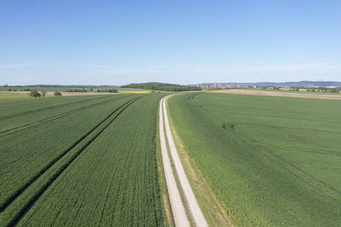 Deutschland, Bayern, Rothenburg ob der Tauber, Luftaufnahme einer unbefestigten Straße, die sich im Sommer durch grüne Felder zieht - RUEF04000