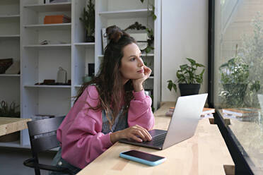 Nachdenkliche Geschäftsfrau sitzt mit Laptop in einem Cafe - SYEF00281