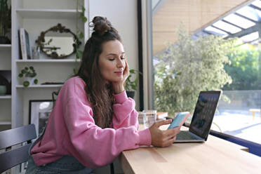 Businesswoman with hand on chin using smart phone at coffee shop - SYEF00285