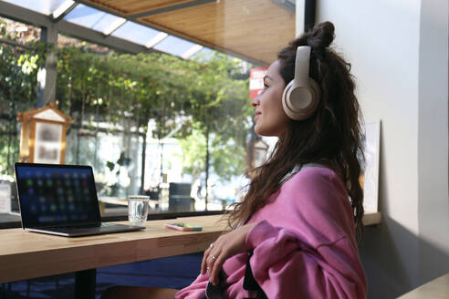 Geschäftsfrau mit drahtlosen Kopfhörern träumt in einem Café - SYEF00289