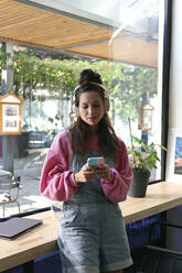 Junger Freiberufler mit Smartphone im Café stehend - SYEF00292