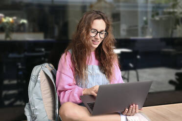 Smiling student working on laptop sitting on bench - SYEF00307