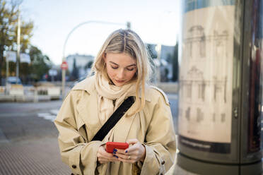 Junge Frau mit blondem Haar benutzt ein Smartphone - JJF00634