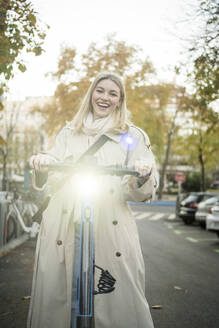 Glückliche Frau mit beleuchtetem Elektro-Scooter auf der Straße - JJF00648