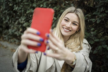 Eine fröhliche Frau macht ein Selfie mit ihrem Mobiltelefon inmitten von üppigem Grün - JJF00659