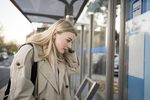 Blonde junge Frau prüft Busfahrplan am Bahnhof - JJF00669