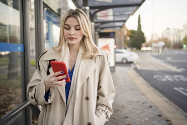 Junge Frau surft an der Bushaltestelle mit ihrem Smartphone im Internet - JJF00672