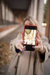 Lächelnde Frau fängt einen Selfie-Moment mit der Frontkamera ihres Smartphones ein - JJF00675