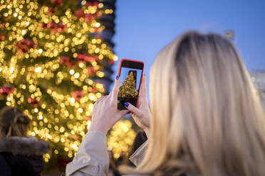 Frau fotografiert nachts den beleuchteten Weihnachtsbaum mit ihrem Smartphone - JJF00676