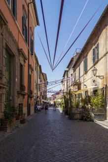 Italy, Lazio, Tuscania, Festival decorations hanging over town street in summer - MAMF02665