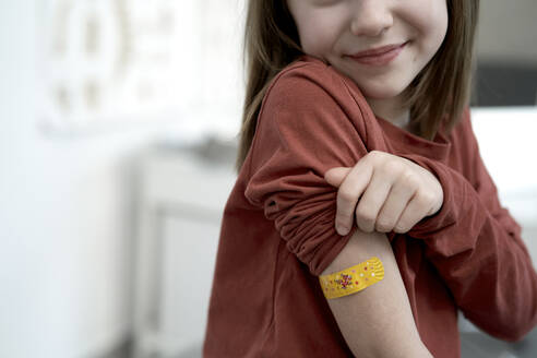 Smiling girl showing adhesive bandage after vaccination in clinic - ABIF01889