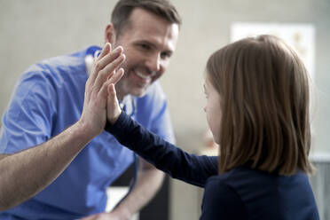 Glücklicher Arzt gibt einem Mädchen in der Klinik ein High-Five - ABIF01891