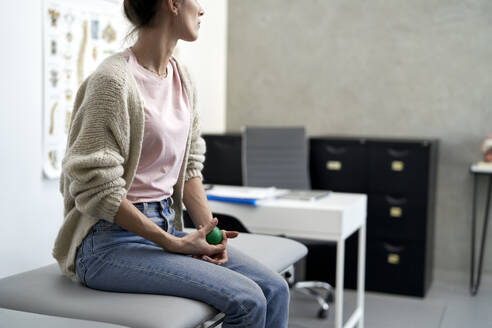 Gestresste Frau sitzt mit einem Stressball auf dem Untersuchungstisch - ABIF01893
