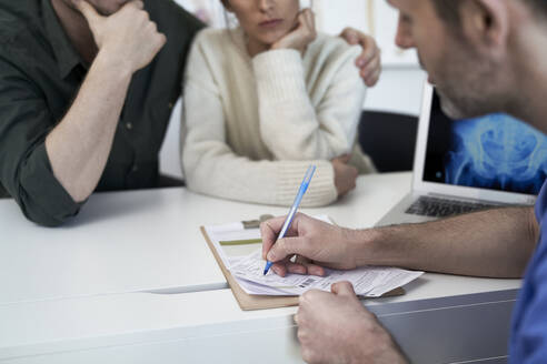 Couple with doctor writing prescription in clinic - ABIF01901