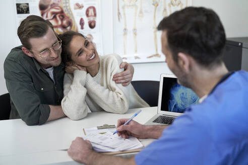 Happy couple with doctor discussing over prescription in clinic - ABIF01902